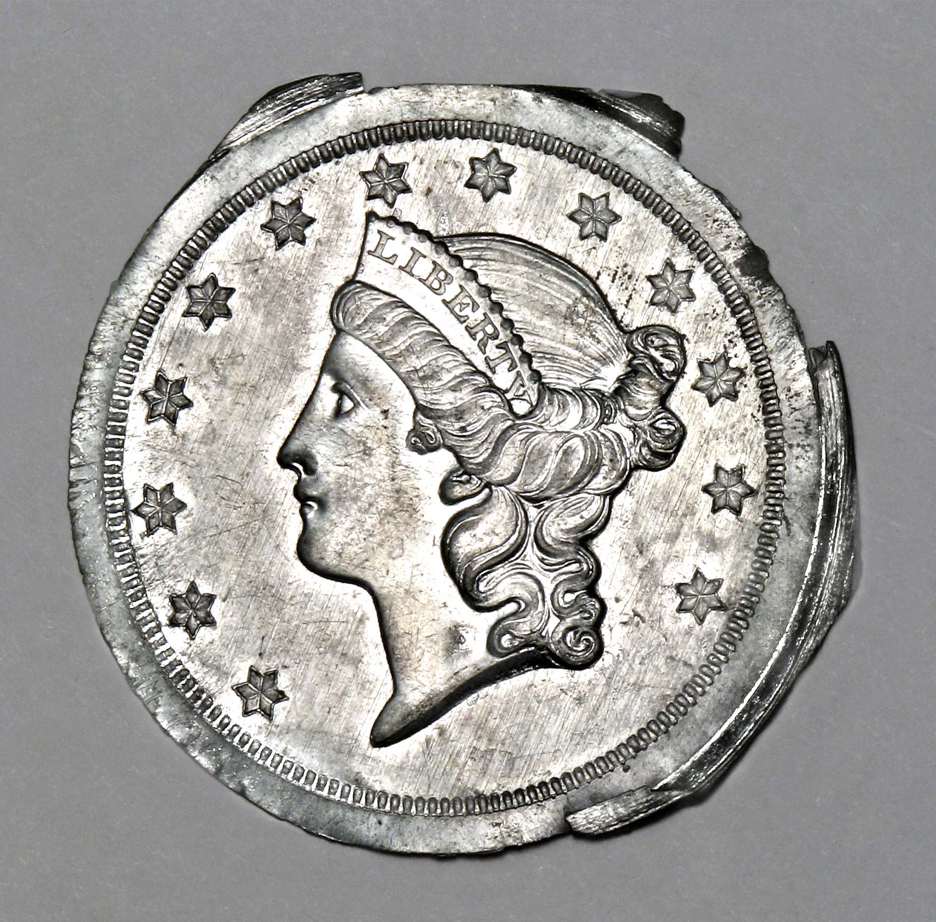 White metal disc impressed with a woman's profile wearing a crown that reads,
