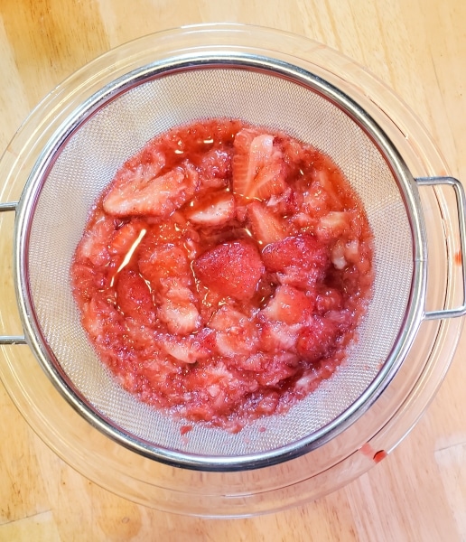 Syrupy strawberry mixture in a strainer over a bowl.