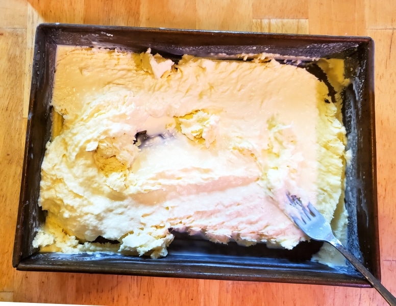 Metal pan filled with frozen cream being mixed with a fork.