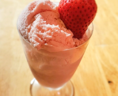 Strawberry ice cream in a glass serving dish with a fresh strawberry.