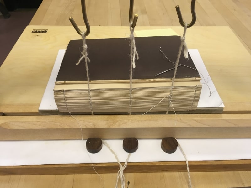 Sewing in progress in a sewing frame, with linen cords.