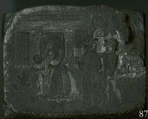 Two white men converse and follow a group of white women and children into a building with the sign Sunday School.