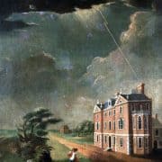 Man walking in a storm while lighting strikes a brick building near trees bending in the wind.