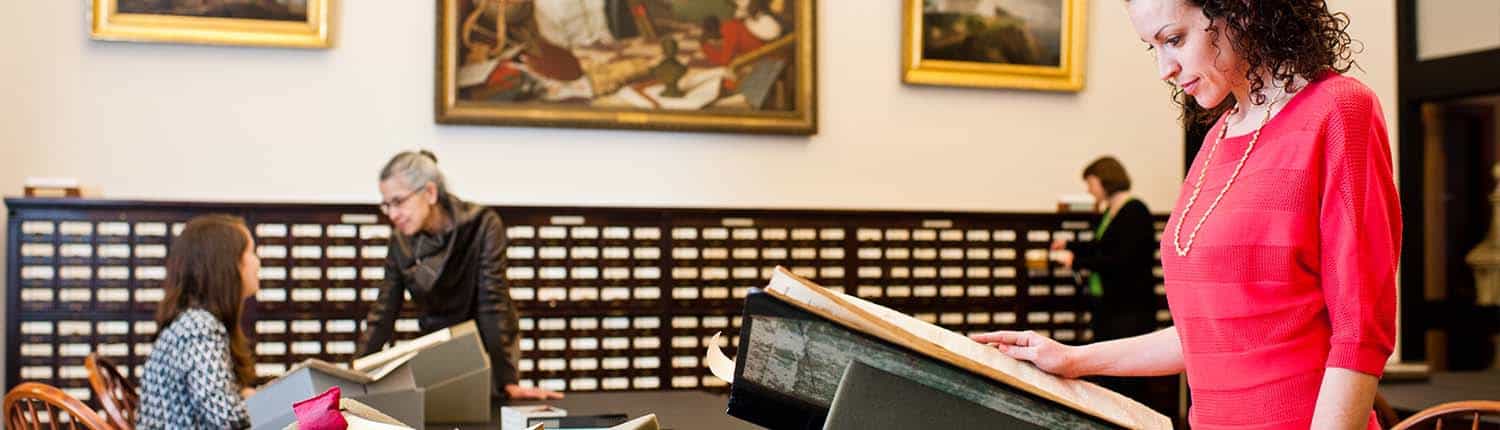 Library Company white woman reference staff and a white woman researcher talk near white women readers looking at large volume and card catalog.