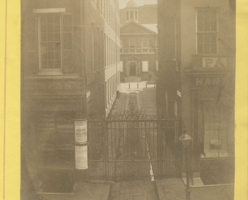 Photograph of Carpenters' Hall visible down a long alleyway, mounted on yellow paper with handwritten notations of place, date, and photographer