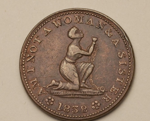 Photograph of medal with woman kneeling with raised arms in chains and text that reads Am I Not a Woman and a Sister 1838