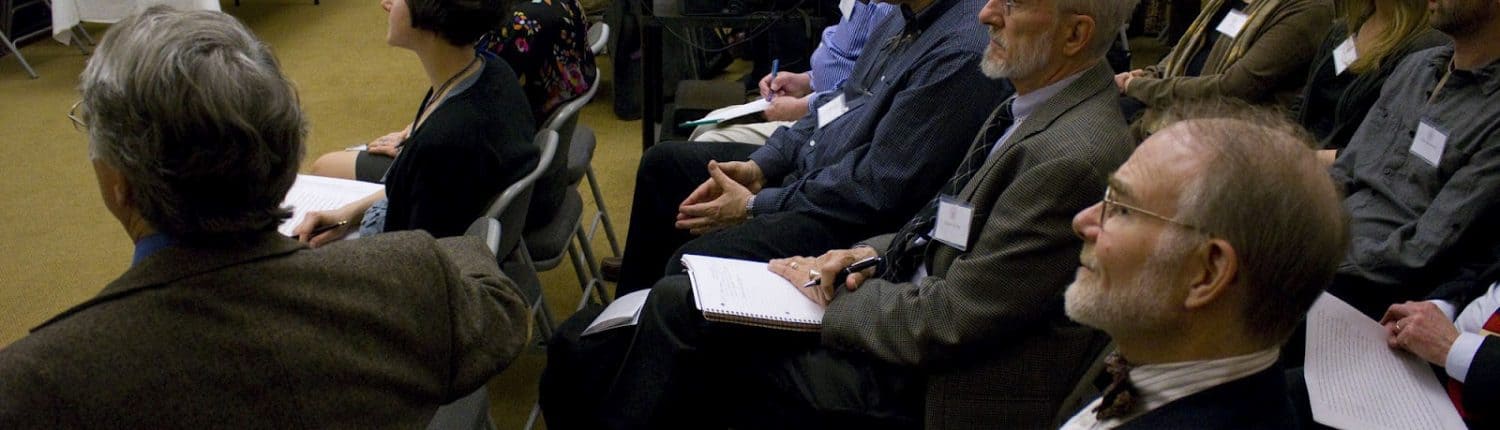 Photograph depicting a crowd of attendees sitting and watching a presentation.